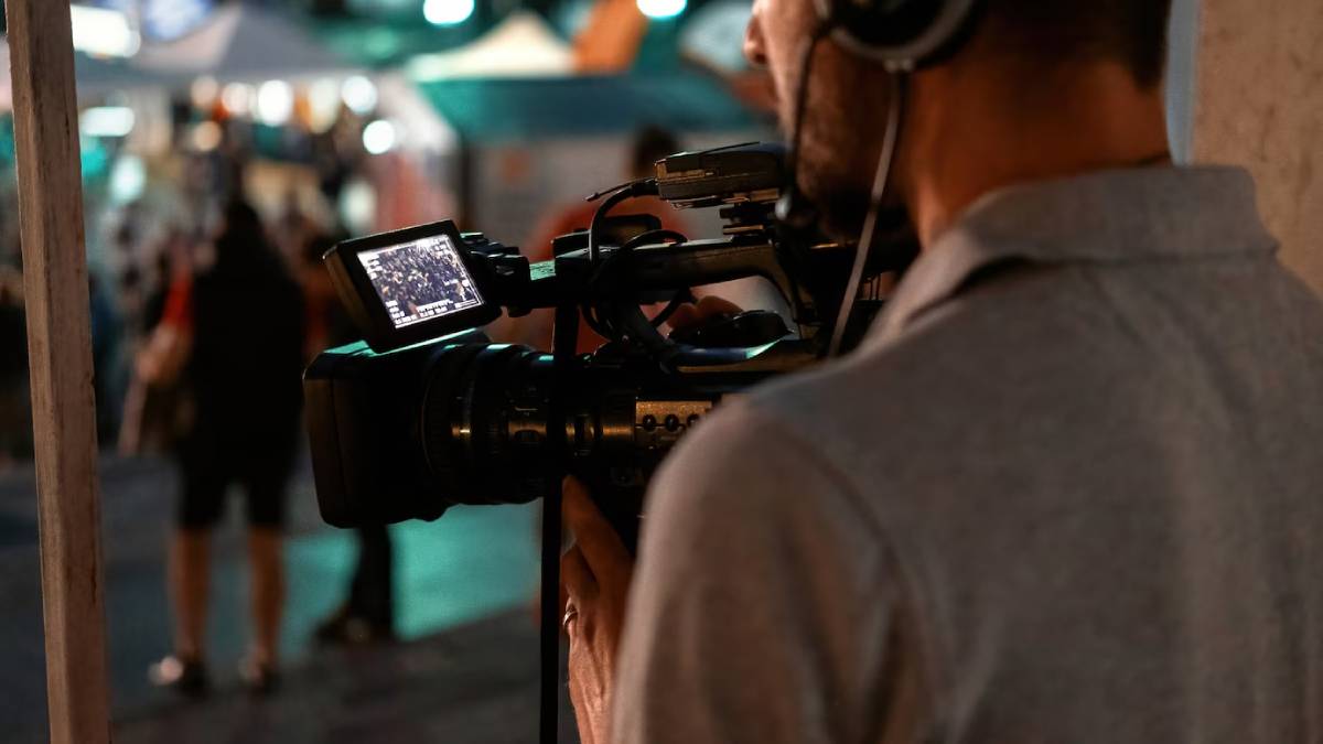 Cameraman operating a professional video camera at a bustling night event, viewing through a monitor.