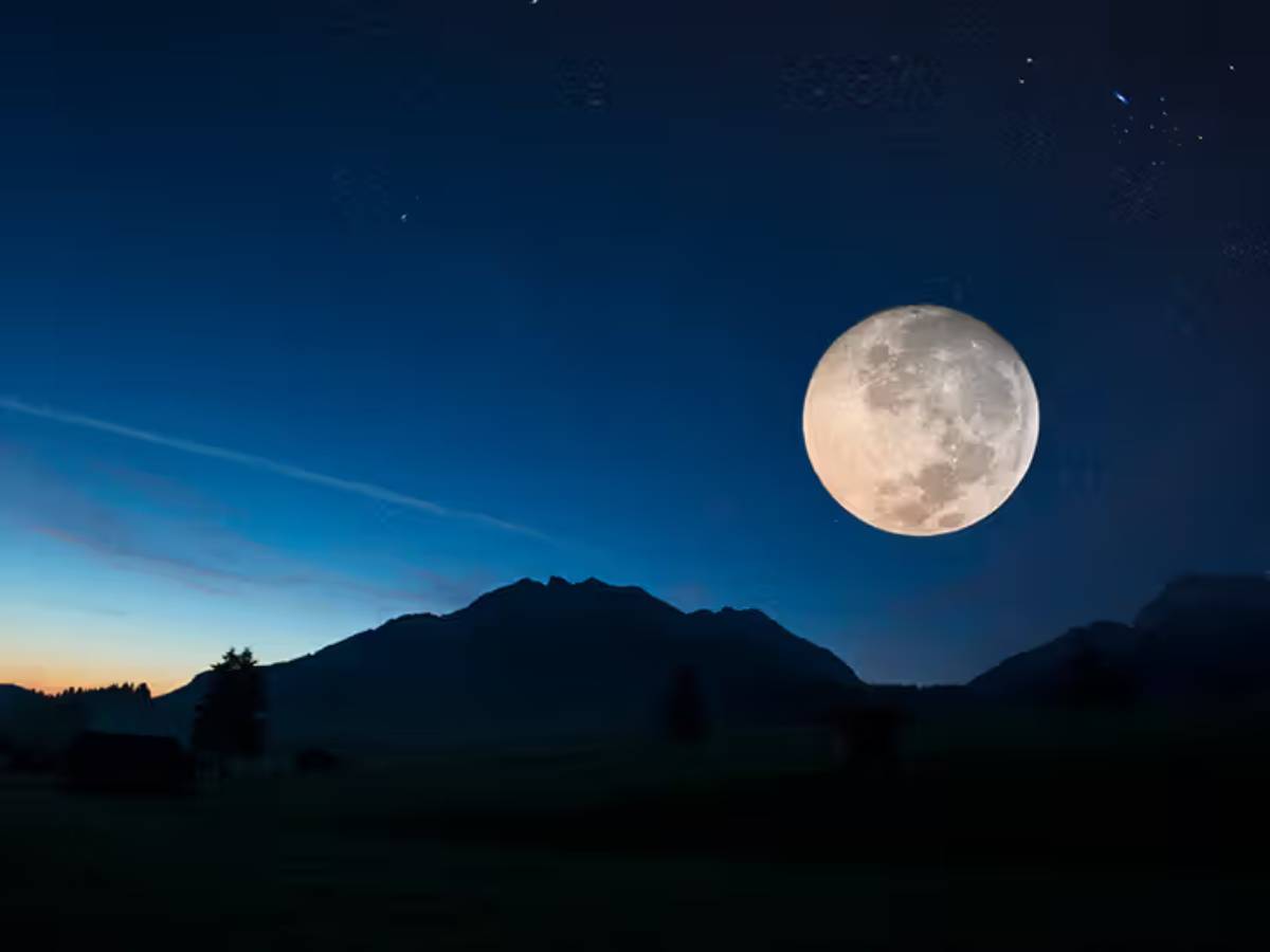 Full moon hanging over a landscape with mountains and a twilight sky.