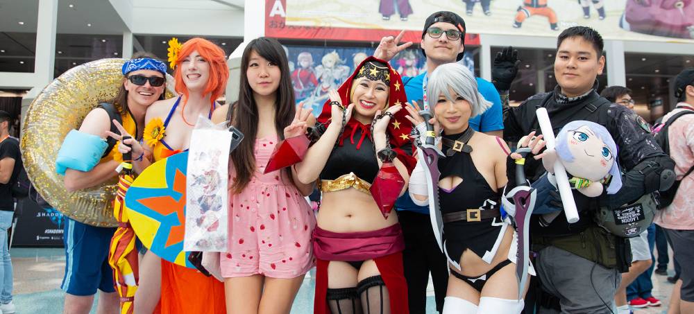 A group of cosplayers in vibrant costumes posing together at a convention, showcasing various characters alongside playful props.