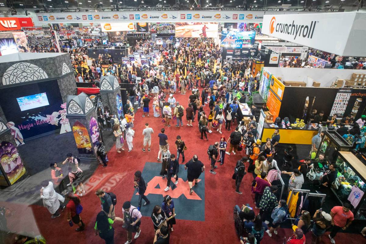A bustling convention hall filled with attendees exploring colorful booths, featuring anime and cosplay displays at a vibrant event.