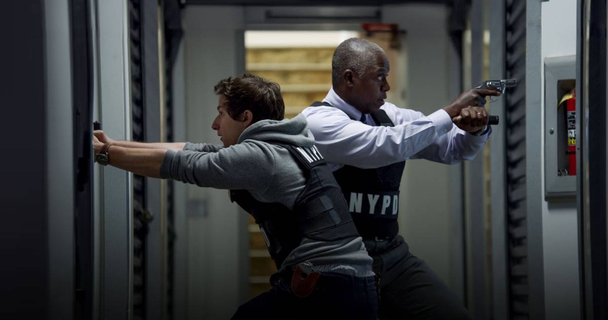 Two individuals in tactical vests are positioned in a corridor, one aiming a gun while the other braces against the wall.
