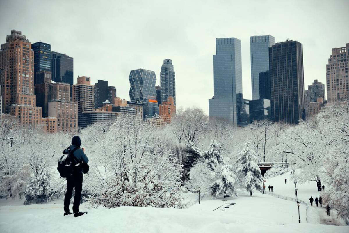 A person observes a snow-covered urban park with skyscrapers in the background.