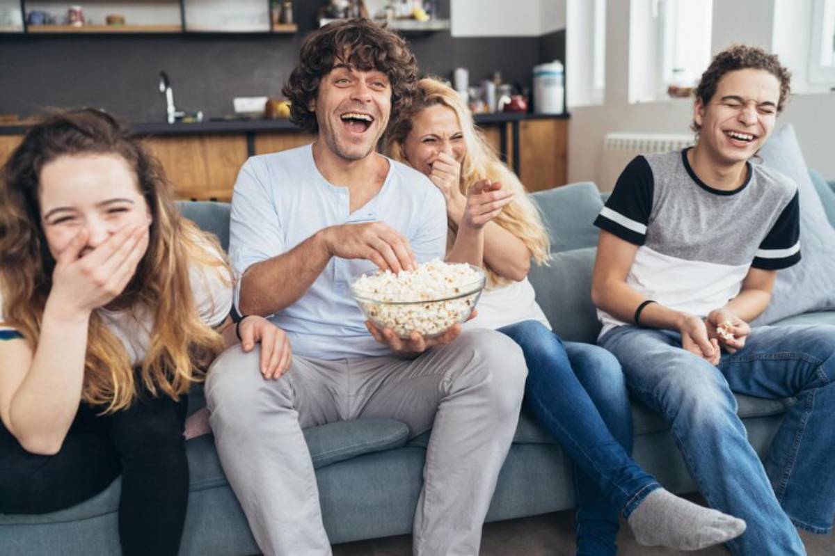 A group of four people on a couch sharing a bowl of popcorn, enjoying a movie night together in a cozy living room.