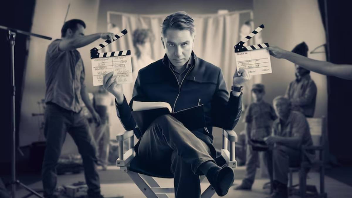 A director sits in a chair on set, holding two clapperboards, while crew members prepare for a scene in the background.