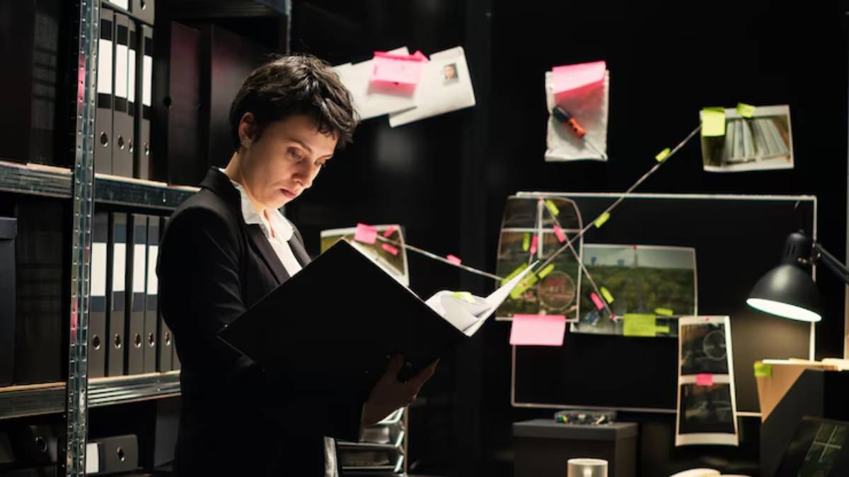 A person in a suit examines a binder in a dimly lit room filled with files, photos, and sticky notes on a dark background.