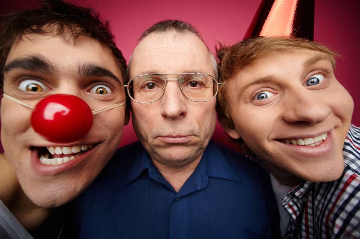 Three people pose close together against a vibrant pink background, celebrating with party hats. Joyful atmosphere with laughter.