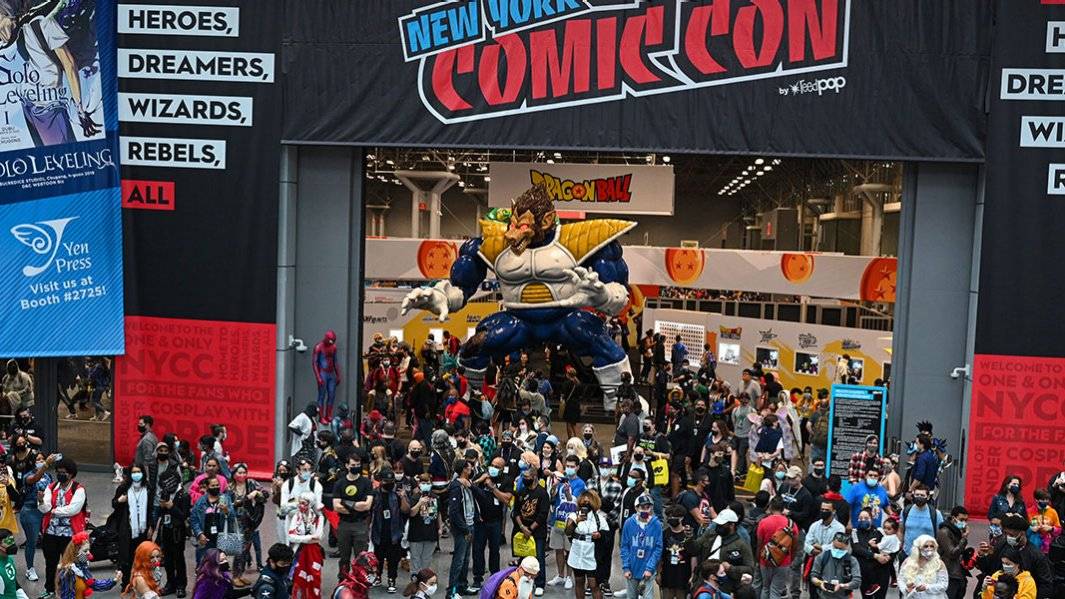 A bustling New York Comic Con scene featuring a large inflatable Dragon Ball character, with attendees in various costumes below.