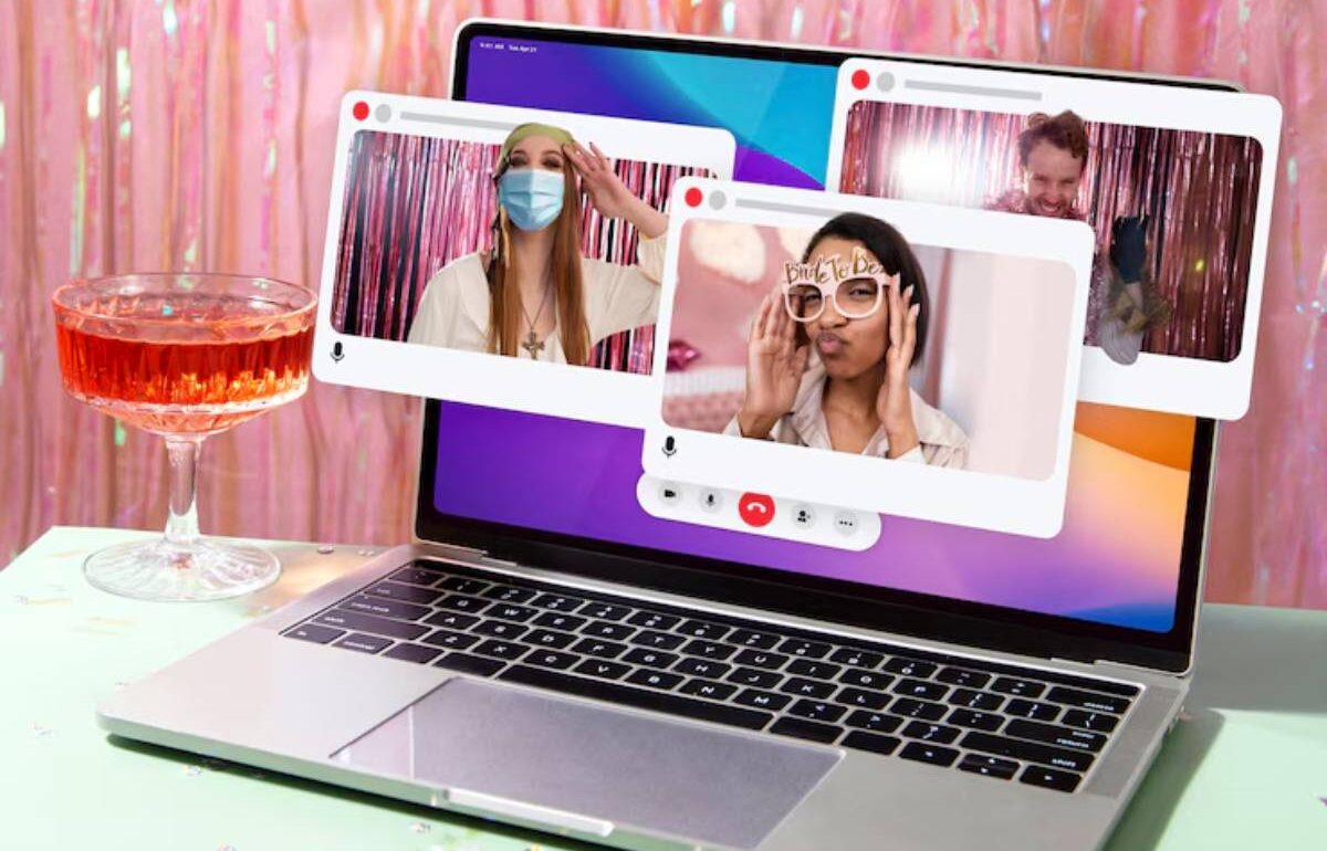 A laptop displays multiple video call windows against a festive backdrop, with a decorative drink nearby on a green table.