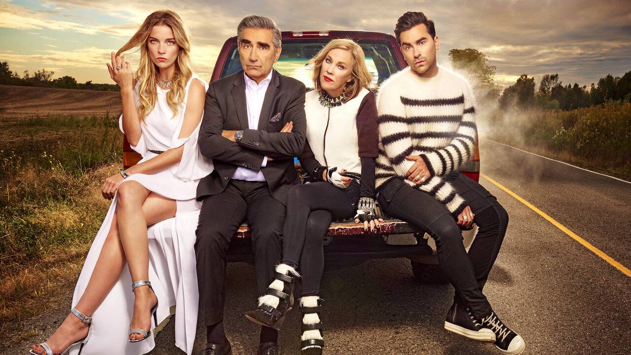 A group of four stylish individuals sit on the back of a pickup truck on a rural road at sunset, exuding a relaxed and fashionable vibe.
