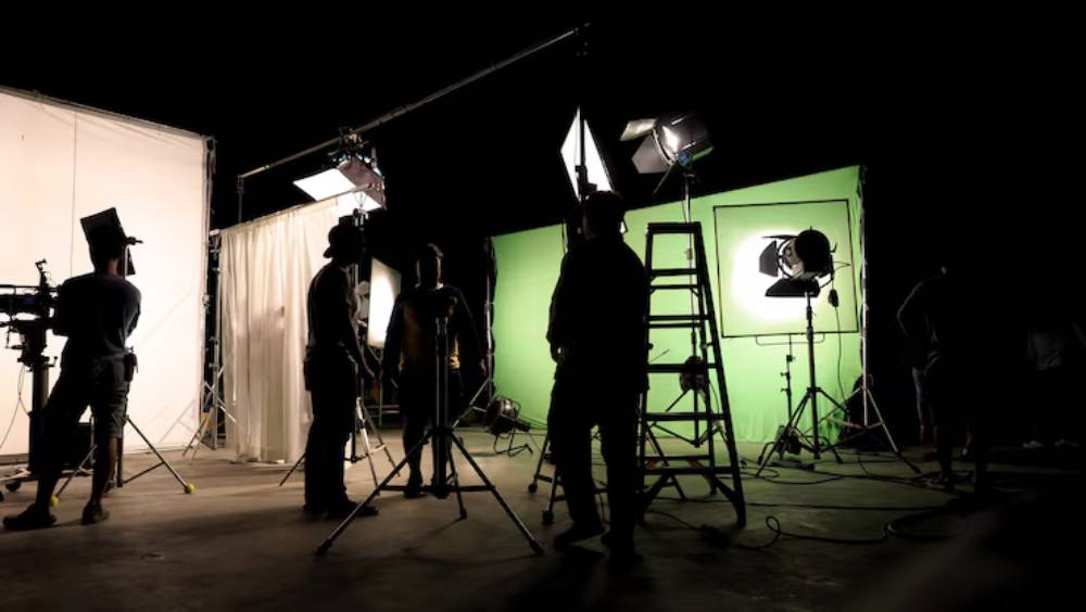 Behind-the-scenes view of a film set featuring lighting equipment, green screen, and crew members preparing for a shoot.